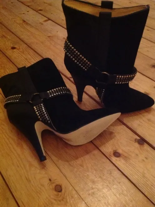 Schwarze Wildleder-Stiefeletten mit hohen Absätzen und besetzten Riemen auf einem Holzboden