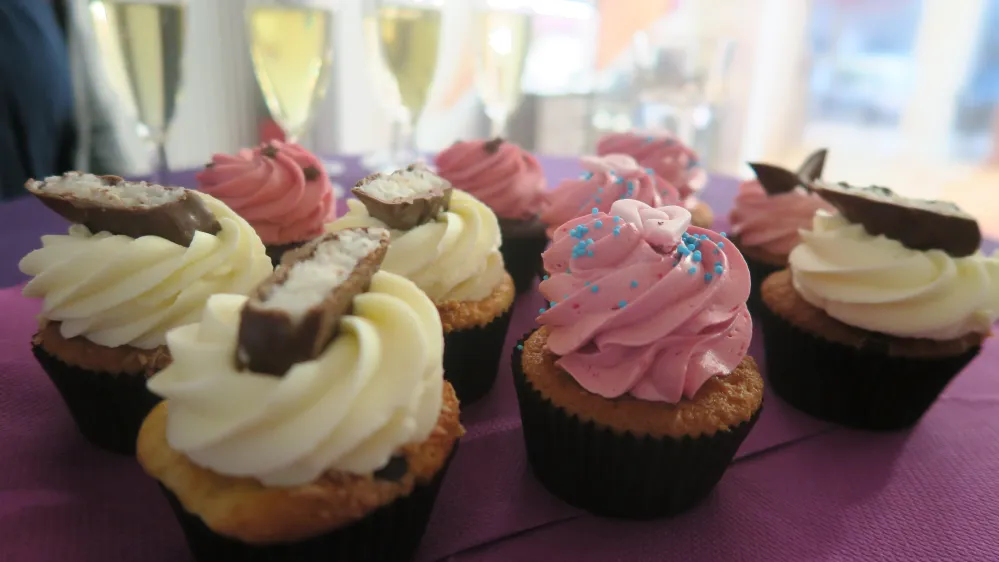 Cupcakes mit rosa und weißer Creme und Schokodekor auf einer violetten Fläche, indoor